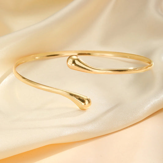 Gold-tone coil arm cuff bangle with two curved ends, sleek open design.
