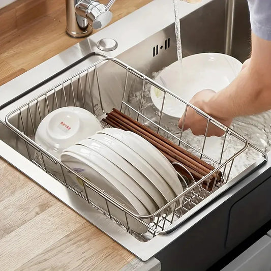Stainless-steel sink dish drying rack holding stacked plates and utensils in a basket