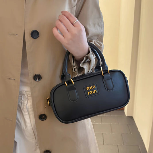 Small black handbag with top handles, front logo patch, and gold-tone zipper trim