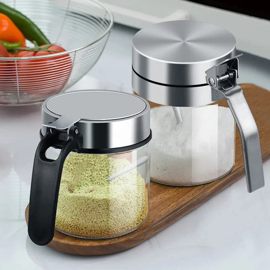 Pair of glass seasoning jars with stainless lids, clear bodies, and built-in spoons