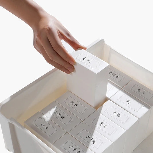 White plastic drawer organizer with labeled compartments, hand lifting a flip lid