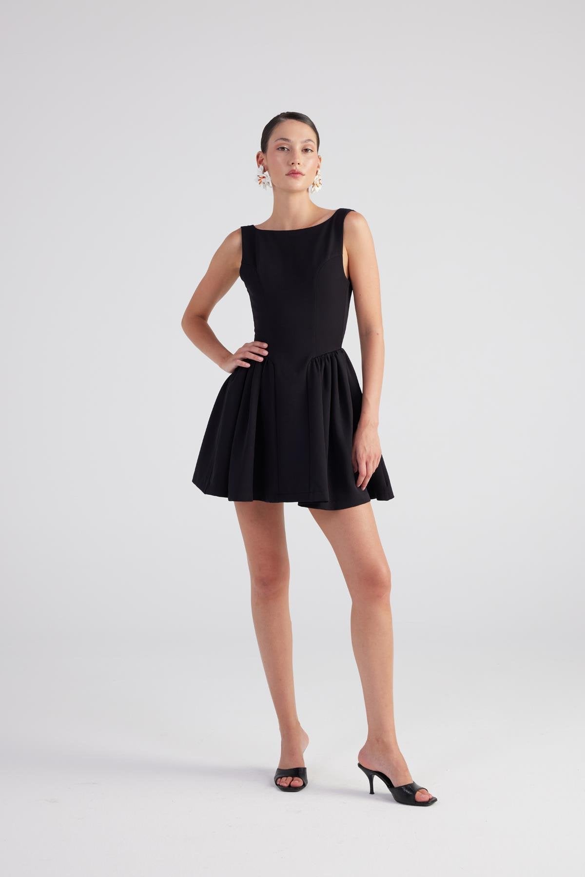 Black sleeveless pleated mini dress in fit-and-flare silhouette with gathered waist