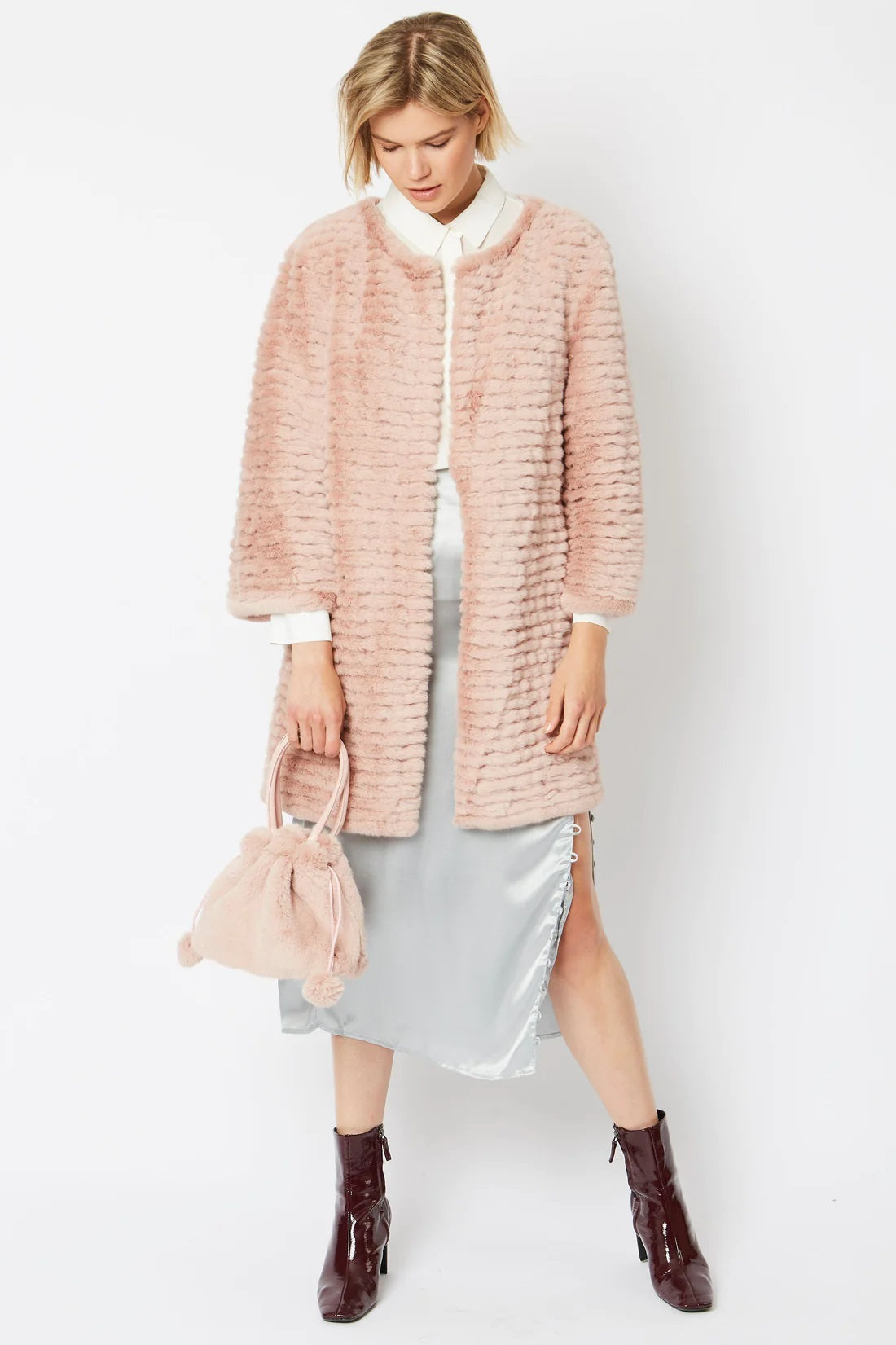 Pink faux fur pom-pom bucket bag with drawstring, held at side