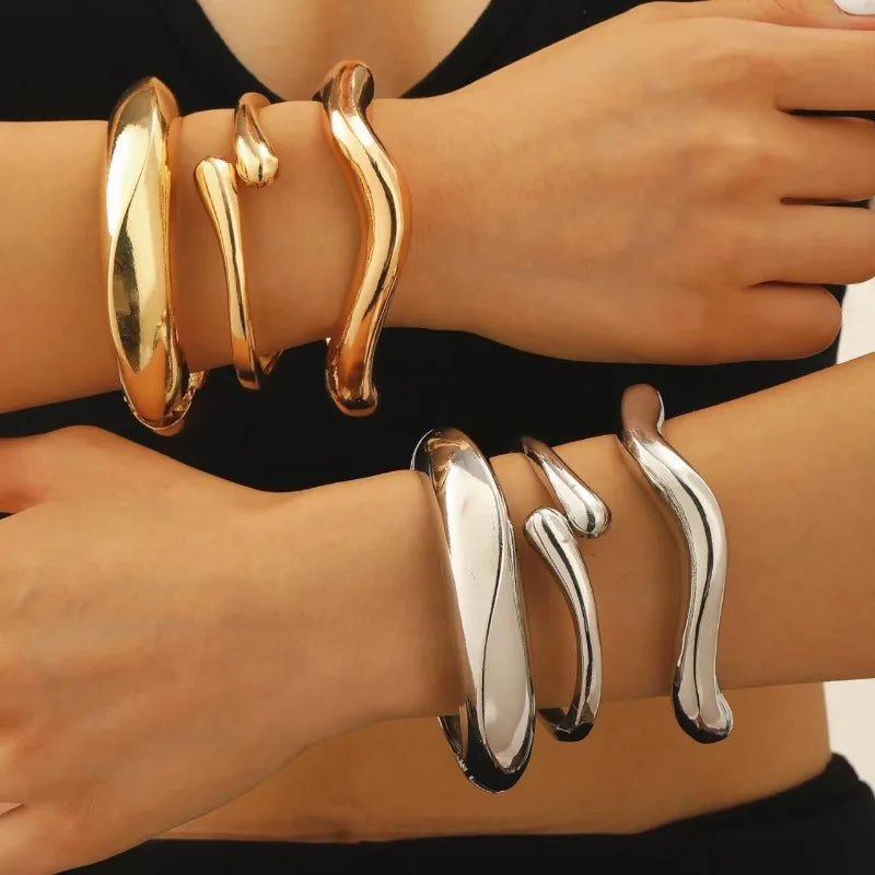 Gold-tone and silver-tone chunky hinged bangles on wrist, smooth oval hoops
