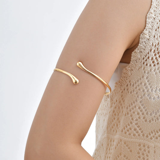 Gold-tone open upper arm bracelet with slim geometric coil ends, adjustable cuff.