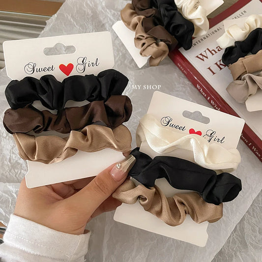 Set of satin hair scrunchies in black, brown, and beige with ruffled fabric