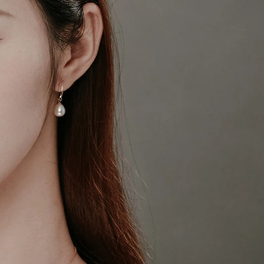 Natural white pearl drop earrings on gold-tone hooks, worn by model