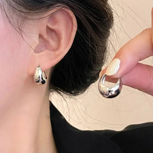 Silver-tone round hoop earrings with glossy curved profile, worn on ear.