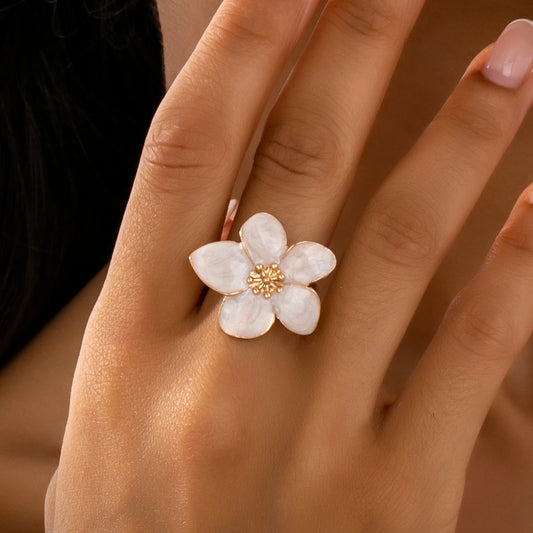 Flower-shaped enamel ring with white petals and gold-tone center on a hand