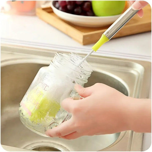 Long-handled bottle brush with white bristles, green cap, and hand scrubbing a jar.