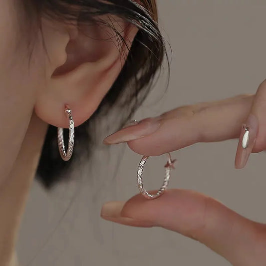 Silver twisted hoop earrings on an ear and a hand showing the hoop shape