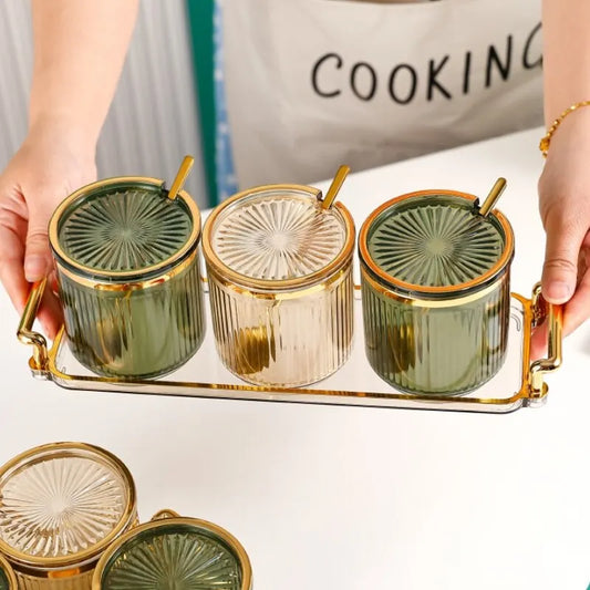 Three glass seasoning jars with gold rims, green and clear bodies, on a metal rack
