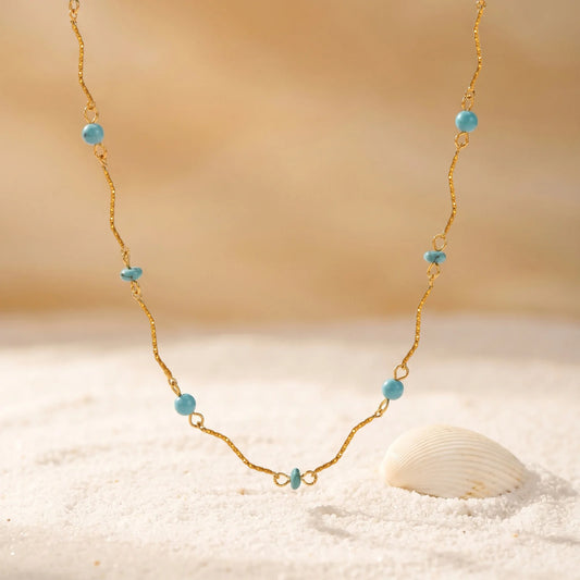 Gold-plated turquoise bead necklace with wavy link chain shown on fabric