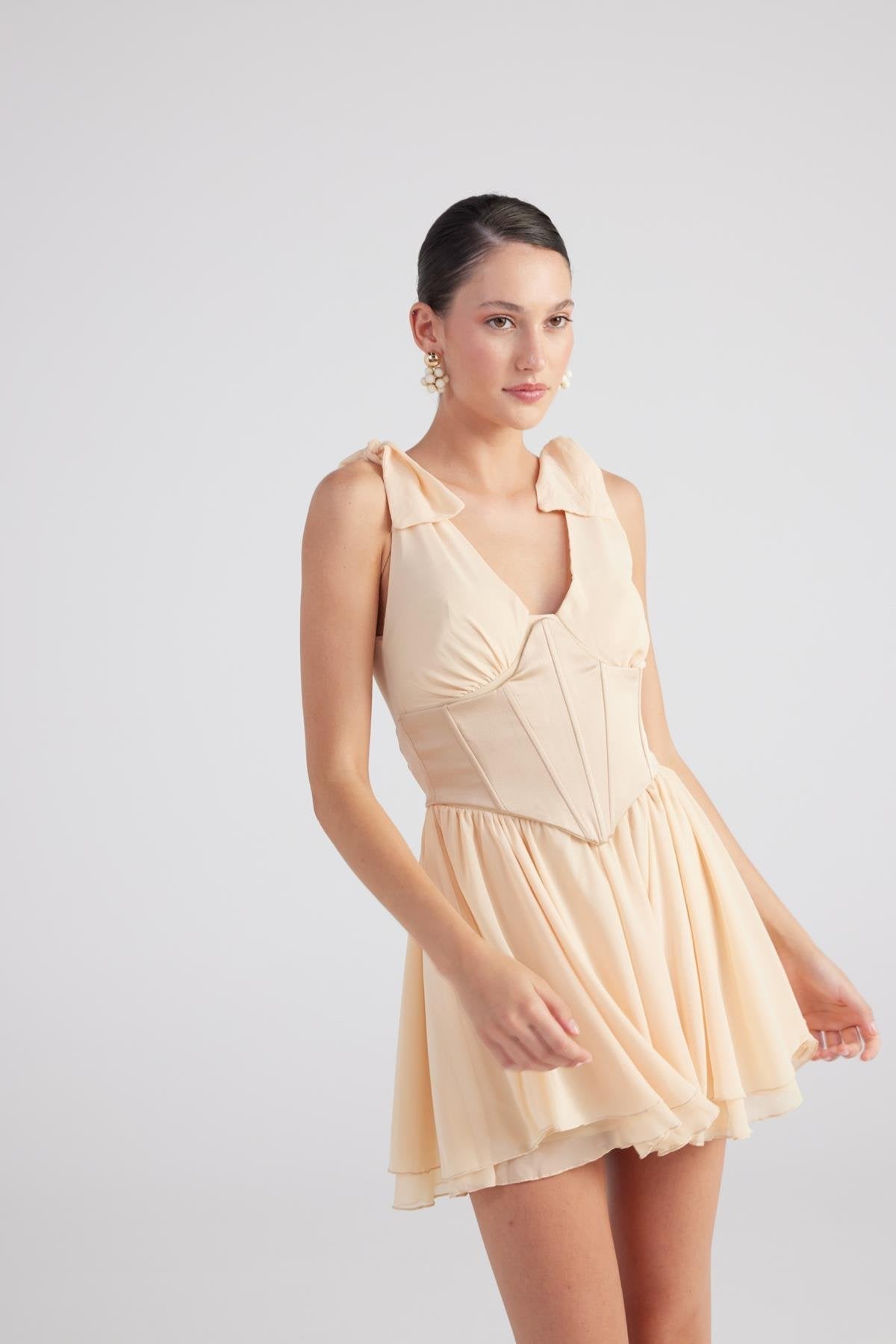 Beige ruched mini dress with V-neck, shoulder ruffles, and pleated skirt