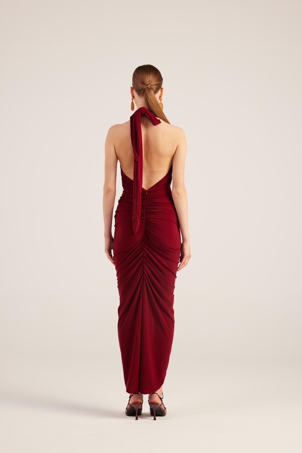 Back view of burgundy backless halter maxi dress with draped ruched detailing