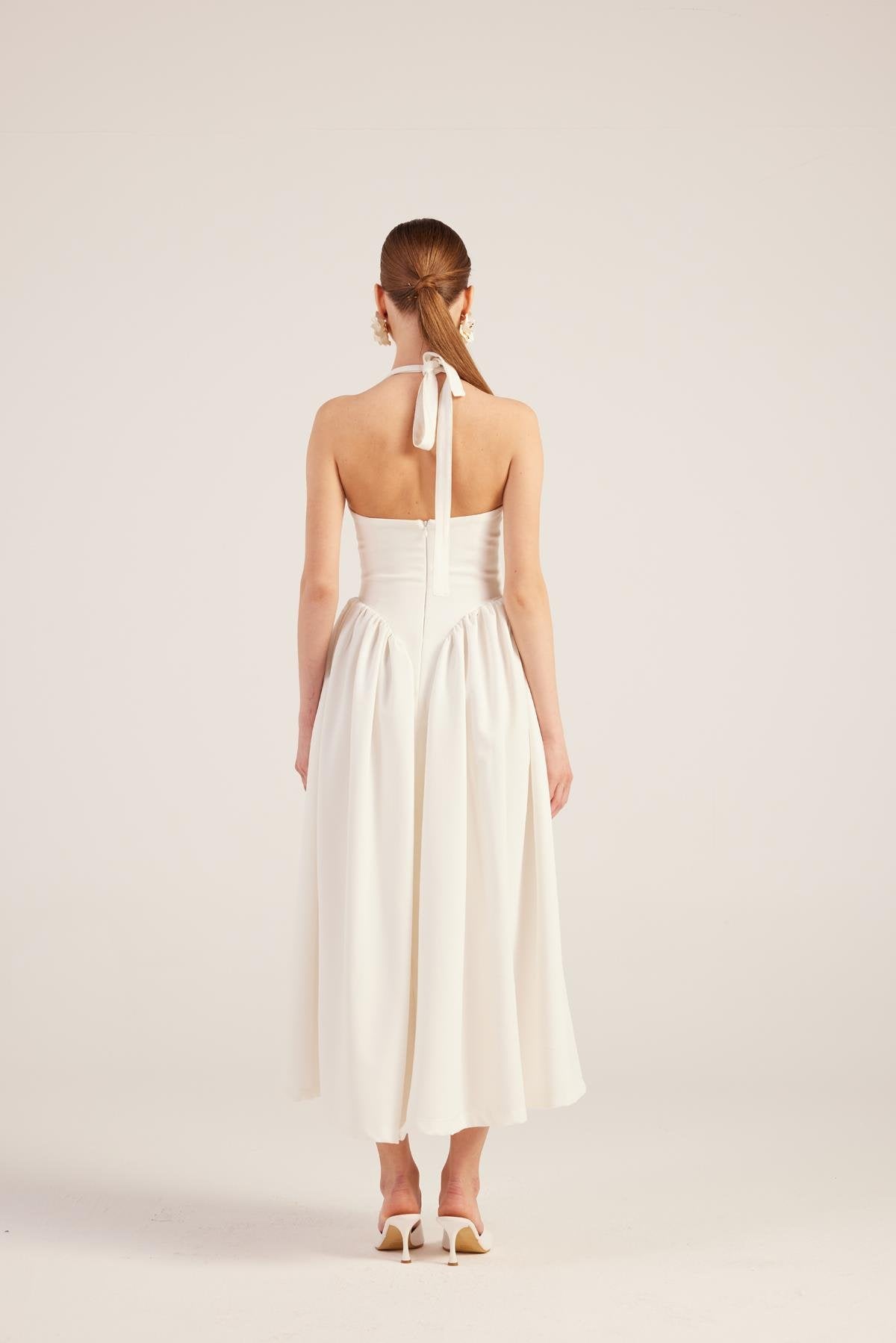 White backless maxi dress with halter tie, V-back opening, and gathered pleated skirt