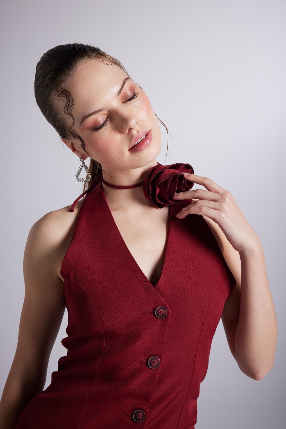 Close-up: burgundy sleeveless dress with V-neck, button details, and rose at collar