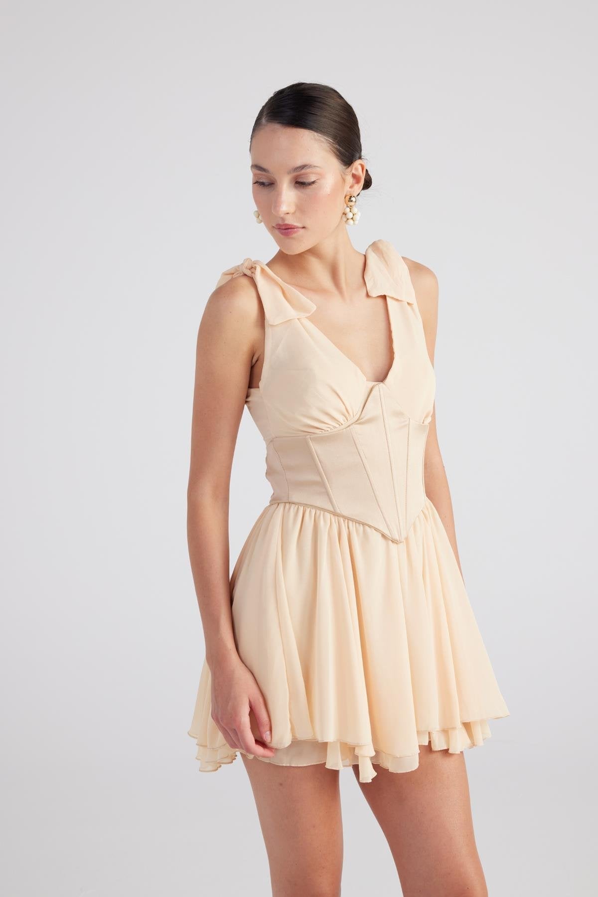 Beige ruched mini dress with V-neck, shoulder ruffles, and pleated skirt