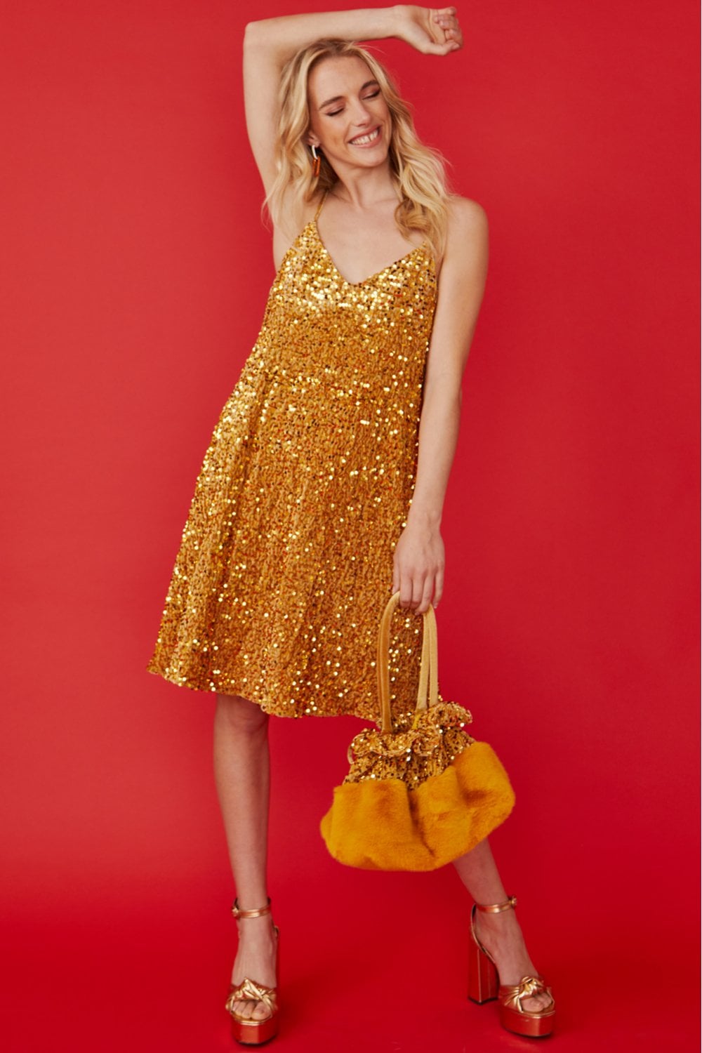 Gold sequin cami dress with V-neck and thin straps, flared hem, holding matching bag